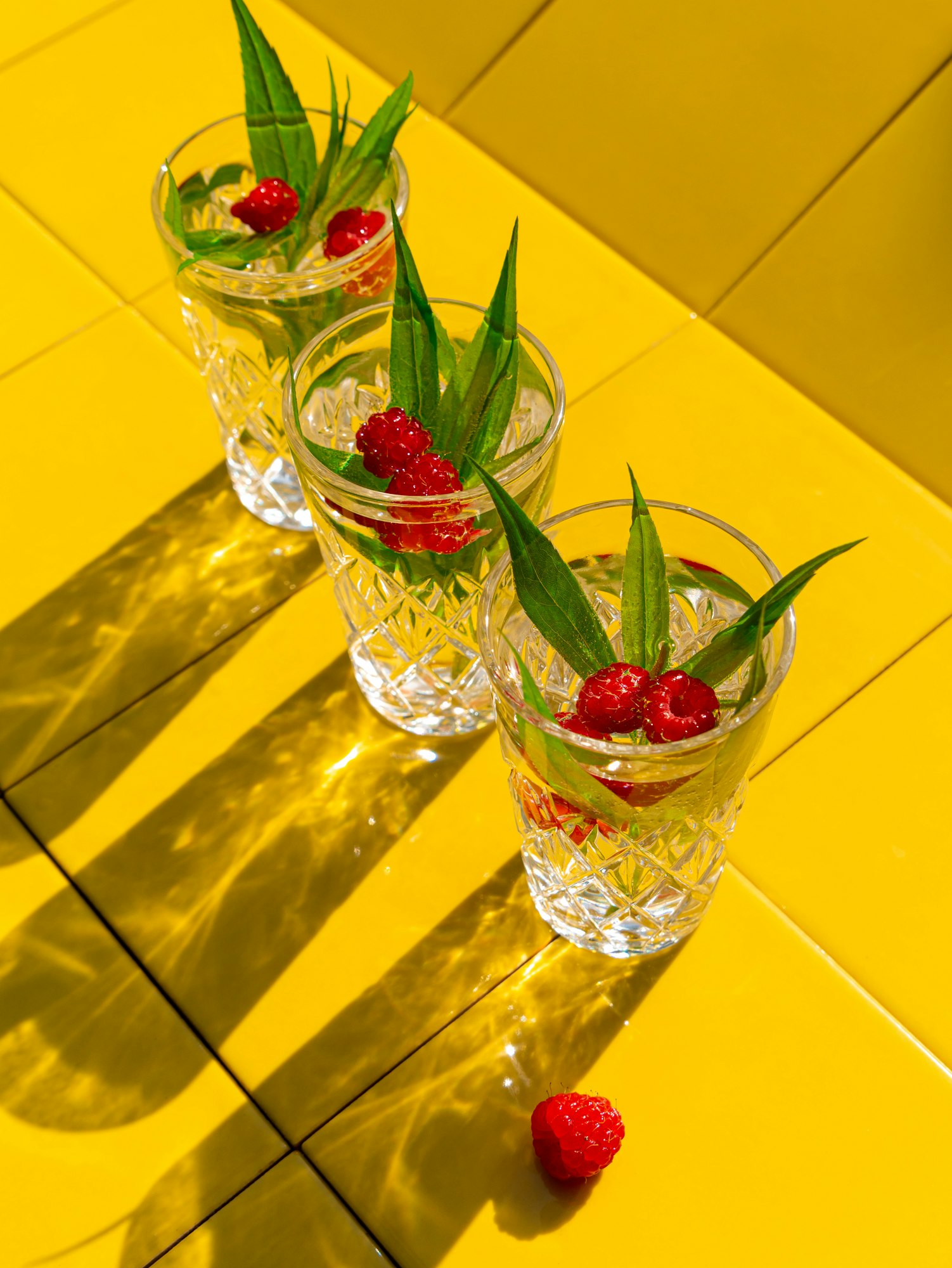 Refreshing summer drinks in crystal glasses green leaves raspberry on yellow tile Sweet cocktails